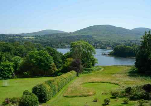beautiful landscape features the manicured gardens and lawns of The Park Hotel Kenmare looking out toward Kenmare Bay and the surrounding hills of County Kerry, Ireland.