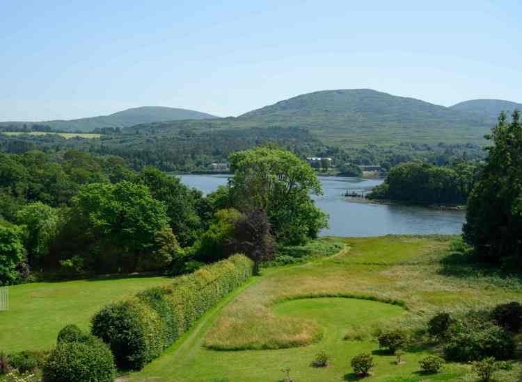 beautiful landscape features the manicured gardens and lawns of The Park Hotel Kenmare looking out toward Kenmare Bay and the surrounding hills of County Kerry, Ireland.