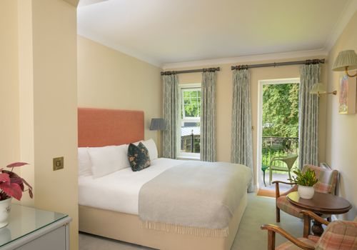 a traditional hotel bedroom at Park Kenmare, decorated in soft cream tones, showcasing a plush double bed with a salmon-pink upholstered headboard and a patterned accent pillow.