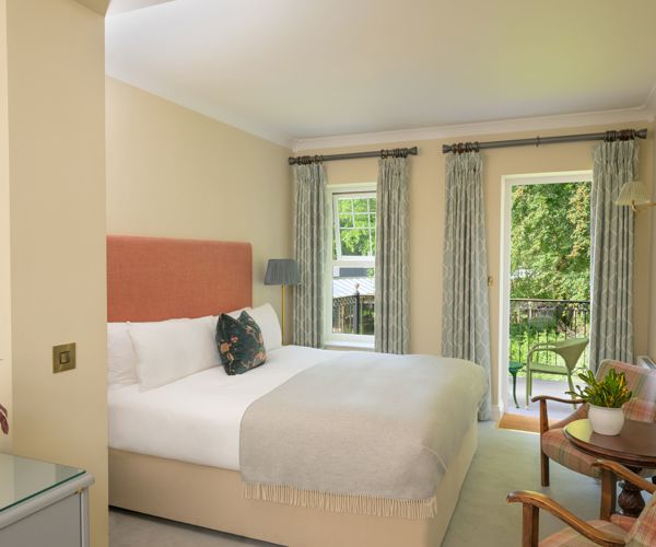 a traditional hotel bedroom at Park Kenmare, decorated in soft cream tones, showcasing a plush double bed with a salmon-pink upholstered headboard and a patterned accent pillow.