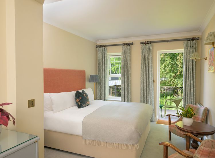 a traditional hotel bedroom at Park Kenmare, decorated in soft cream tones, showcasing a plush double bed with a salmon-pink upholstered headboard and a patterned accent pillow.