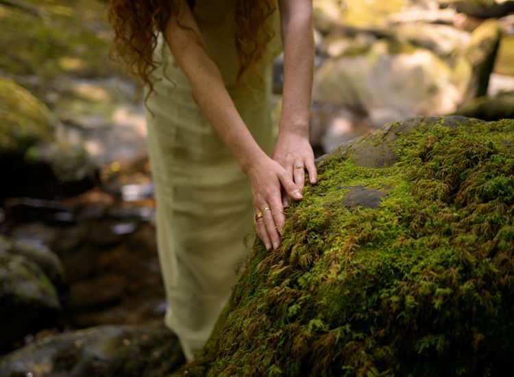 a serene, nature-inspired lifestyle moment focusing on a person gently placing their hands upon a large, vibrant green moss-covered rock in a forest setting